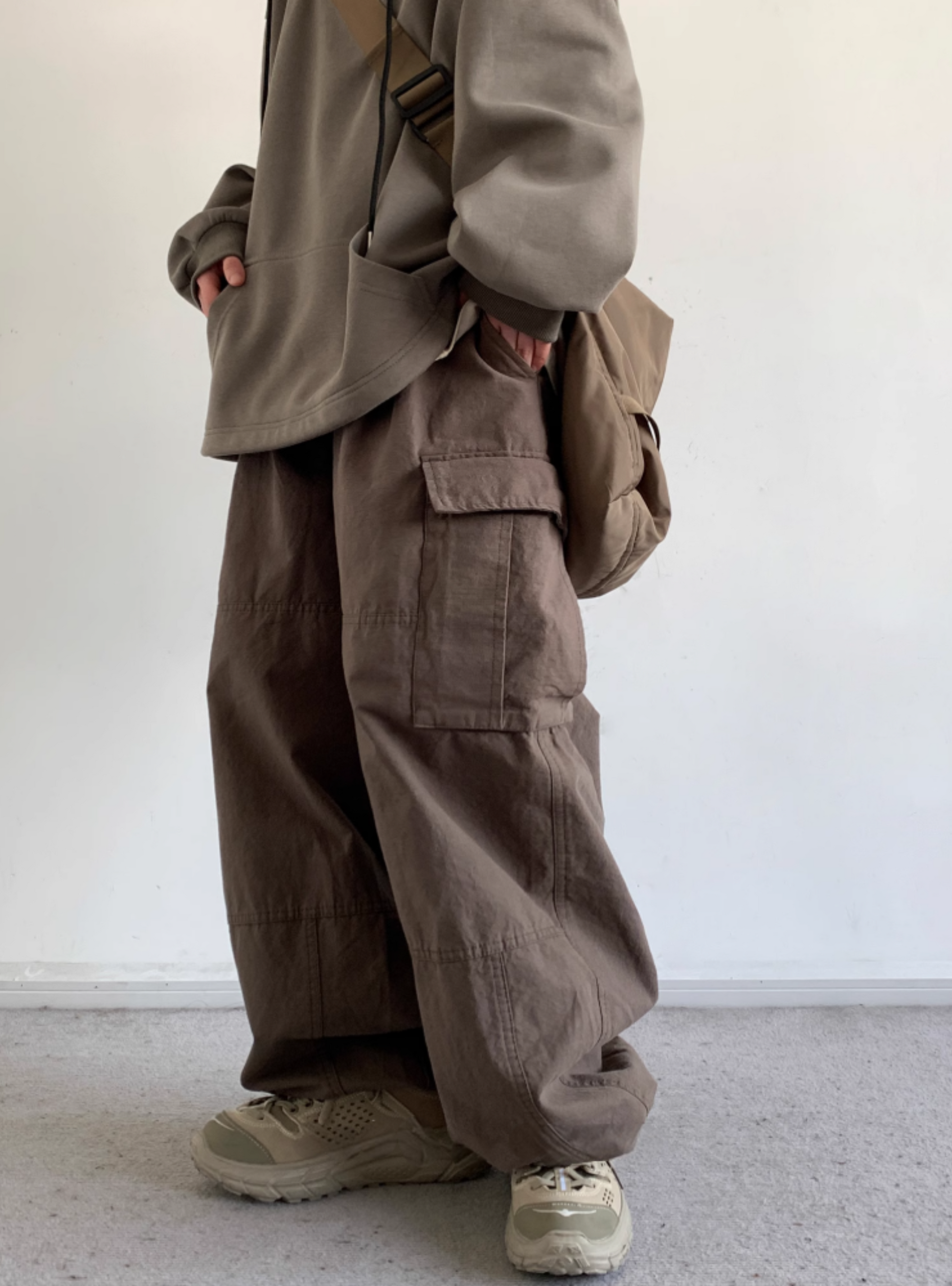 A person standing against a white background, wearing gray utility cargo pants with a wide fit and straight-leg silhouette, featuring multiple pockets.